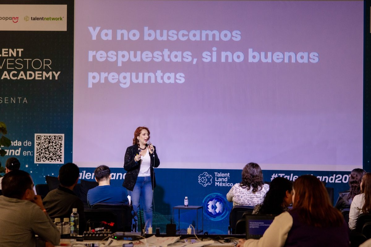 Ingrid en el escenario de Talent Land México, frente al público, con la frase “Ya no buscamos respuestas, sino buenas preguntas” en pantalla